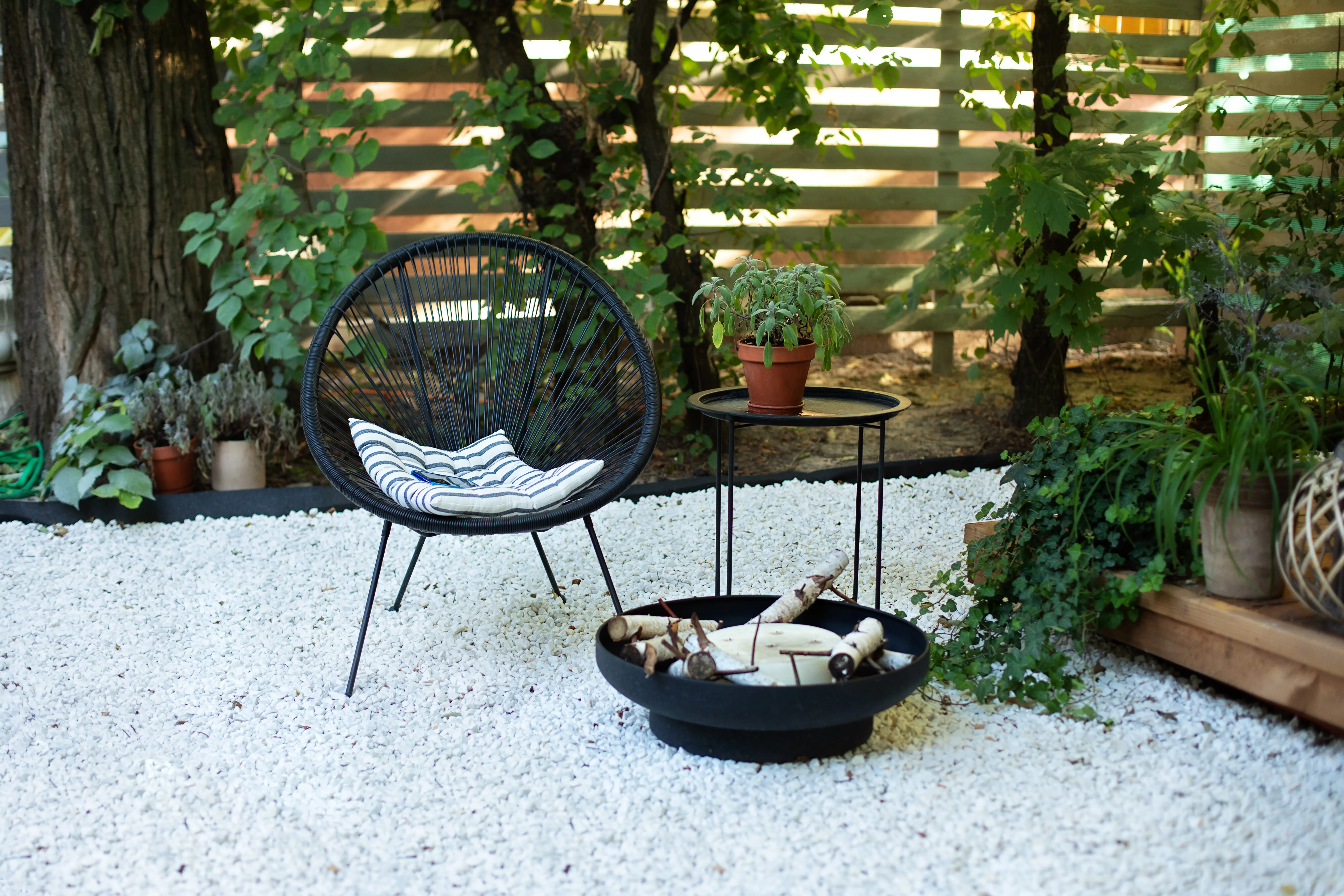 An outdoor house veranda with two black Acapulco armchairs, a coffee table, and plant pots.